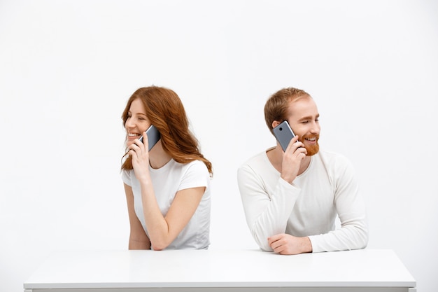 Fröhliches Mädchen und Mann, die am Telefon sprechen, sitzen zusammen