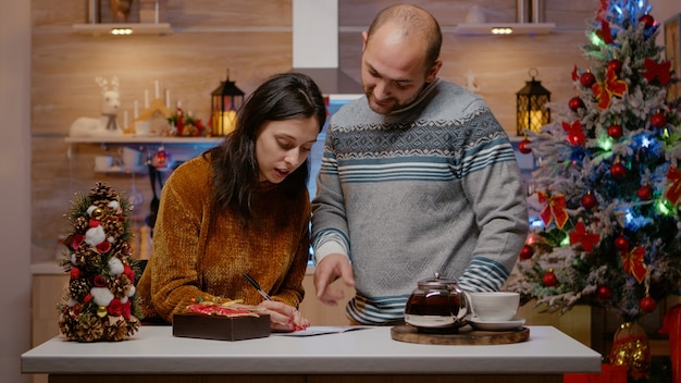 Fröhliches Paar bereitet Geschenk- und Weihnachtskarte vor