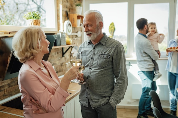 Fröhliches reifes Paar, das vor dem Familienessen in der Küche mit Wein anstößt. Der Mensch steht im Fokus.