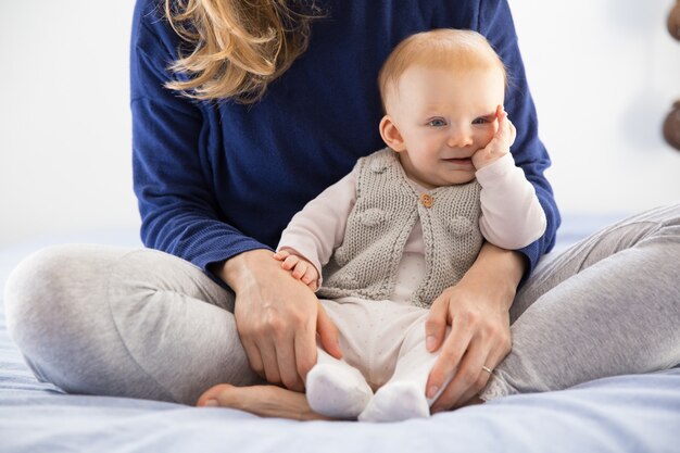 Fröhliches rothaariges Baby, das in den Armen der Mutter sitzt