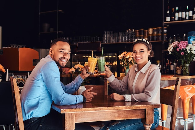 Fröhliches schönes afroamerikanisches verliebtes Paar, das eine tolle Zeit zusammen in einem Restaurant bei ihrer Verabredung hat, ein attraktives Paar, das sich amüsiert, hält Gläser Saft.