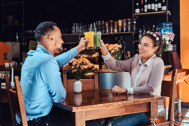 Fröhliches schönes afroamerikanisches verliebtes Paar, das eine tolle Zeit zusammen in einem Restaurant bei ihrer Verabredung hat, ein attraktives Paar, das sich amüsiert, hält Gläser Saft.