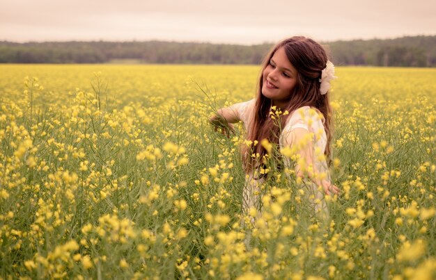 Fröhliches schönes Kind, das in einem Feld der gelben Blumen geht und Natur genießt