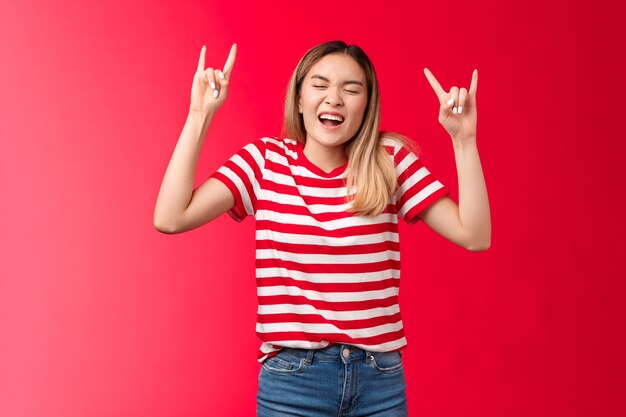 Fröhliches wildes rücksichtsloses blondes asiatisches mädchen, das spaß hat, die kontrolle zu verlieren, die rocknroll-zeichen zeigt, genießen sie...