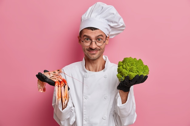 Froh, dass professioneller Koch ungekochten Crefish und Brokkoli hält, glücklich, etwas Neues in Essen zu verbreiten, kocht in der Küche