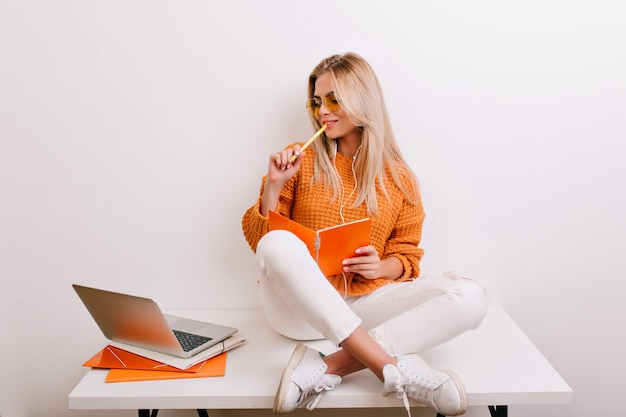 Frohe blonde Frau im trendigen Outfit, die ihren Job im Büro macht und Notizbuch und Stift hält