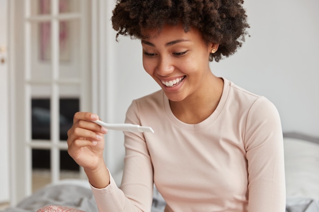 Frohe Frau schaut Schwangerschaftstest an