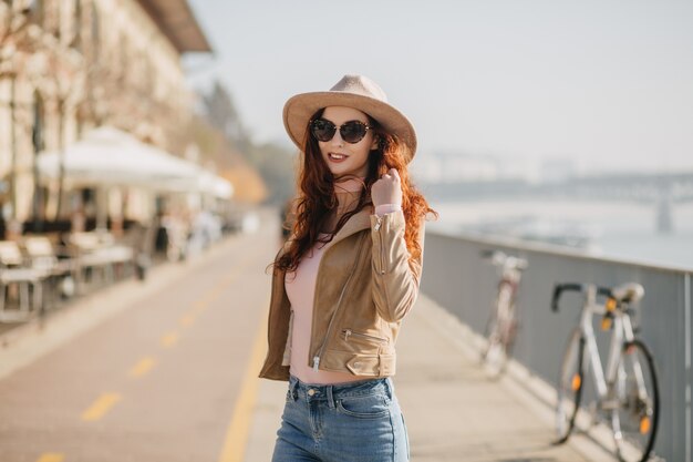 Frohe junge Dame trägt beige Hut und Jacke, die positive Gefühle ausdrücken