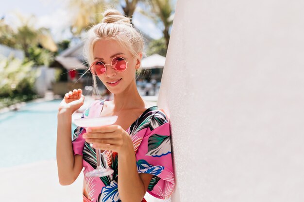 Frohe junge Frau im trendigen Kleid, das im Resort chillt.