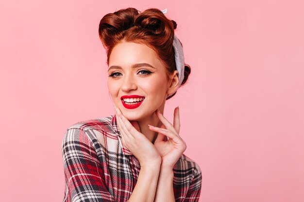 Frohe junge Frau im Weinlese-Outfit, das an der Kamera lächelt. Studioaufnahme der wunderschönen Pinup Lady mit roten Lippen.