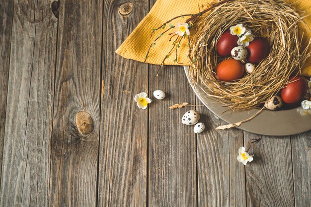 Frohe Ostern Tisch. Ostereier in einem Nest auf einer Metallplatte auf einem Holztisch. Frohe Ostern Konzept