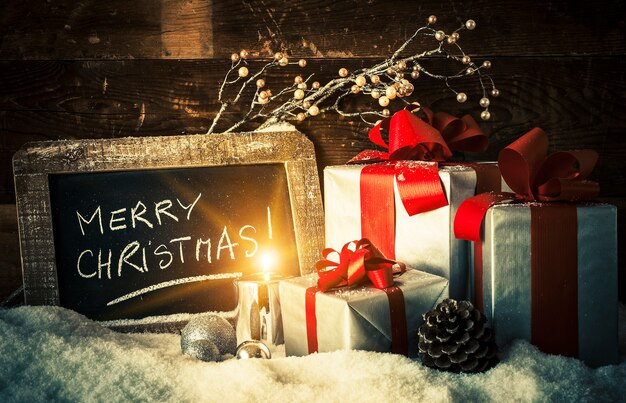 Frohe Weihnachten auf einer Tafel mit Geschenken und Kerze.