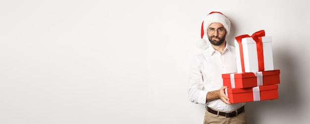 Kostenloses Foto frohe weihnachten ferien konzept nachdenklicher mann, der weihnachtsgeschenke hält und misstrauisch in die kamera schaut