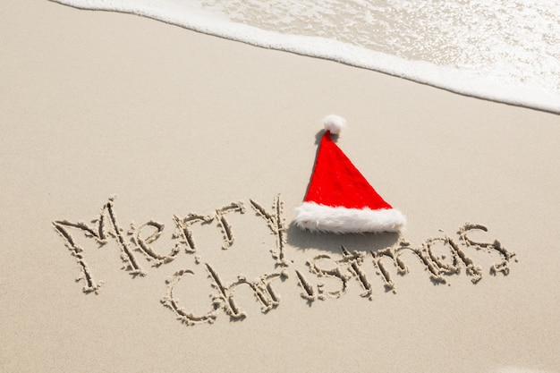 Frohe Weihnachten mit Sankt-Hut auf Sand geschrieben