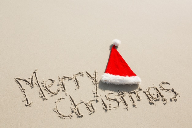 Frohe Weihnachten mit Sankt-Hut auf Sand geschrieben