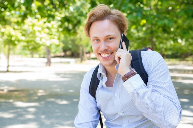 Froher glücklicher Studentenkerl, der um Telefon im Park ersucht