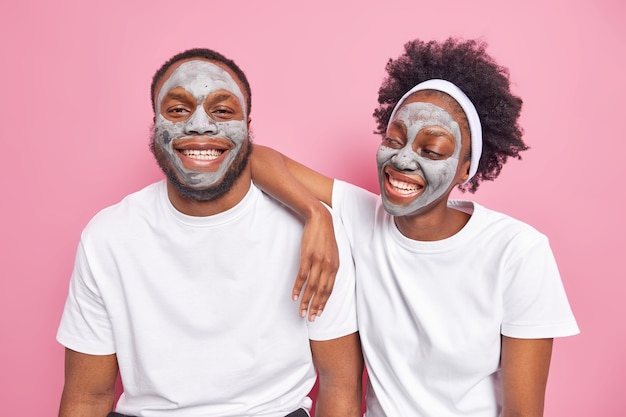 Frohes afroamerikanisches Paar wendet eine Ton-Gesichtsmaske für das Gesichtspflegelächeln an