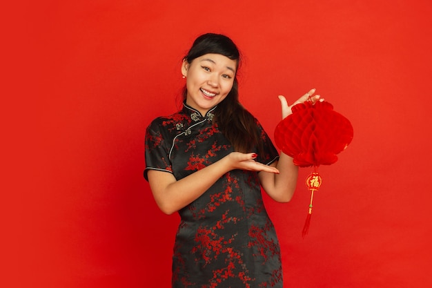 Frohes chinesisches neues jahr 2020. porträt des asiatischen jungen mädchens lokalisiert auf rotem hintergrund. weibliches modell in traditioneller kleidung sieht glücklich aus und lächelt mit dekoration. feier, urlaub, emotionen.