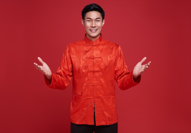 Frohes chinesisches neues Jahr. Schöner asiatischer Mann mit offener Handgeste der Einführung isoliert auf rotem Hintergrund.