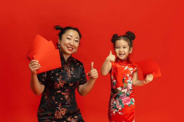 Frohes chinesisches Neujahr. Asiatisches Mutter- und Tochterporträt lokalisiert auf roter Wand