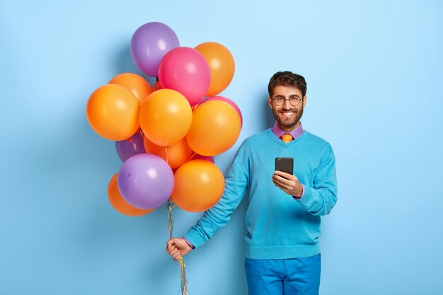 Frohes Kerl mit Luftballons, die im blauen Pullover aufwerfen