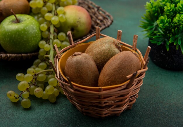 Frontalansicht Kiwi in einem Korb mit grünen Trauben und Äpfeln auf einem grünen Hintergrund