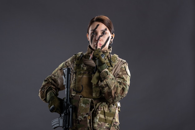 Frontansicht Soldatin mit Maschinengewehr in Tarnung auf grauer Wand