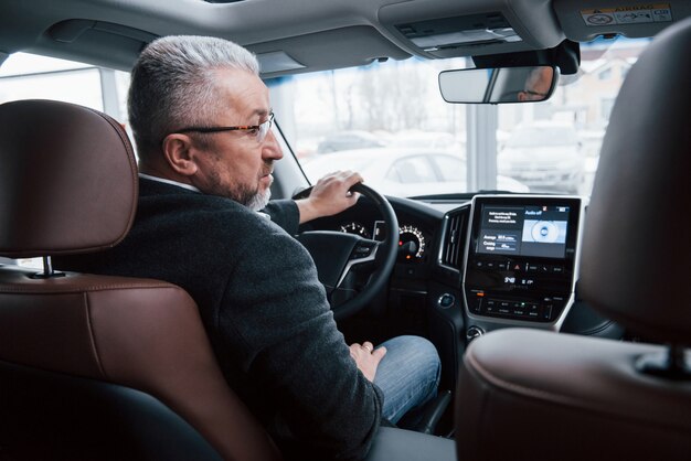 Frontgeräte sind eingeschaltet. blick von hinten auf einen älteren geschäftsmann in offizieller kleidung, der ein modernes neues auto fährt