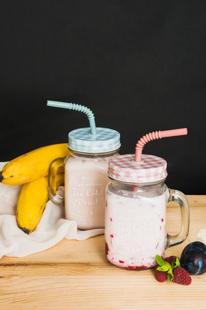 Frucht-Smoothies in geschlossenem Glas mit blauen und rosa Strohen gegen schwarzen Hintergrund