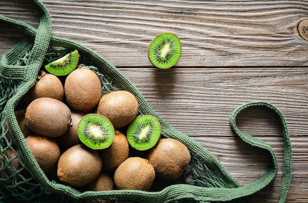 Kostenloses Foto früchte der kiwi in einer maschentasche auf einem rustikalen stil der hölzernen hintergrunddraufsicht