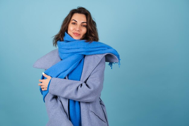 Frühlings-Herbst-Porträt einer Frau in einem blauen Strickpullover, Schal und grauem Mantel, die fröhlich posiert, lächelnd, in Erwartung des Frühlings