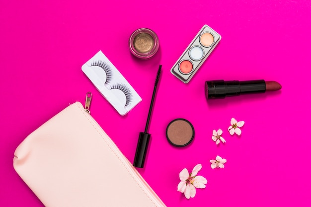 Frühlingsblüte; Wimpern; Lidschatten; Lippenstift; Wimperntuschenbürste und -blüte mit rosa Make-uptasche auf rosa Hintergrund