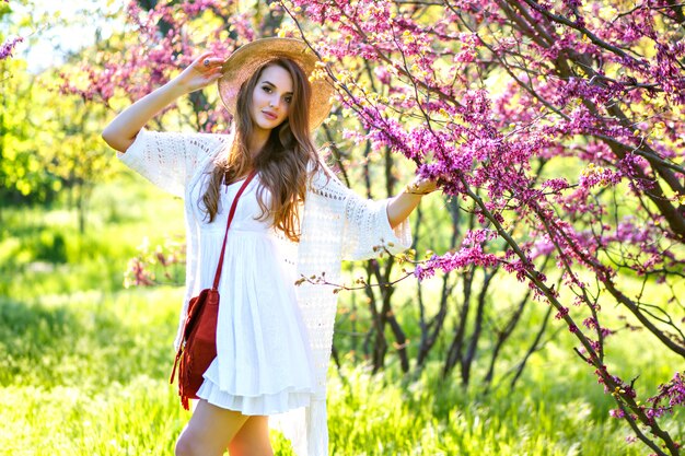 Frühlingsmodeporträt des eleganten Modells, das am blühenden Sakura-Park aufwirft, genießen sonnigen warmen Tag