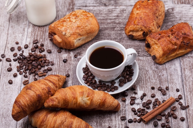 Frühstück mit frischen Coissants mit Kaffee und Milch auf rustikalem Holztisch. Goldenes Croissant.