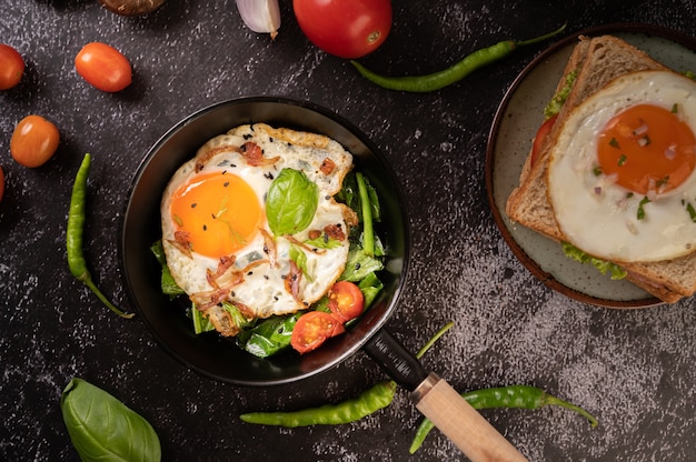 Frühstück mit Spiegeleiern, Wurst und Schinken in einer Pfanne mit Tomaten. Chili und Basilikum