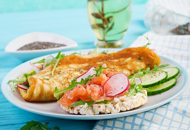 Frühstück. Omelett mit Radieschen, grünem Rucola und Sandwich mit Lachs auf weißem Teller. Frittata - italienisches Omelett.