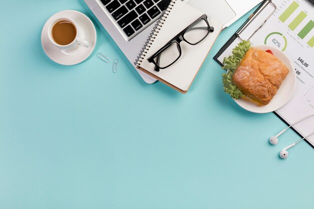 Frühstücken Sie mit gewundenem Notizblock, Laptop, Brillen, Kopfhörern auf blauem Schreibtisch