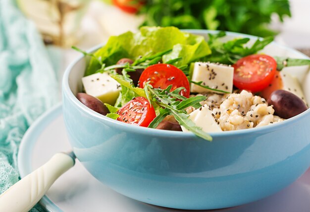 Frühstücksschüssel mit Haferflocken, Tomaten, Käse, Salat und Oliven