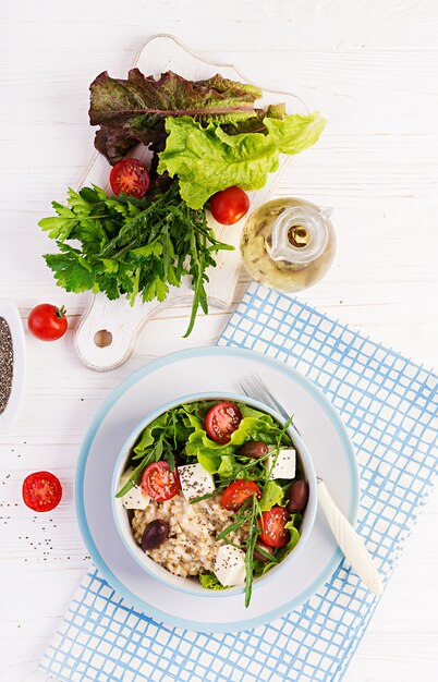 Frühstücksschüssel mit Haferflocken, Tomaten, Käse, Salat und Oliven