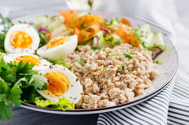 Frühstücksschüssel mit Haferflocken, Zucchini, Salat, Karotte und gekochtem Ei