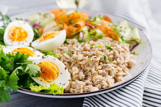 Frühstücksschüssel mit Haferflocken, Zucchini, Salat, Karotte und gekochtem Ei