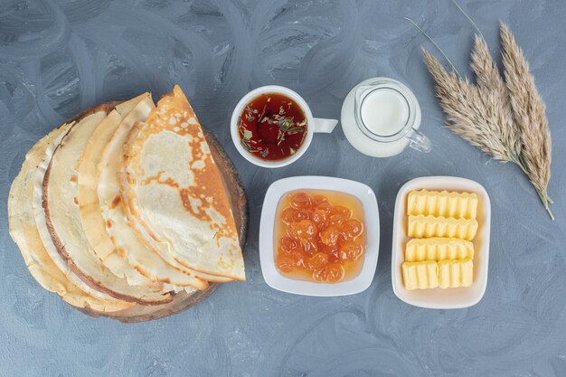 Frühstücksset aus Pfannkuchen, weißer Kirschmarmelade, Butter, Tasse Tee und Milch auf Marmoroberfläche.