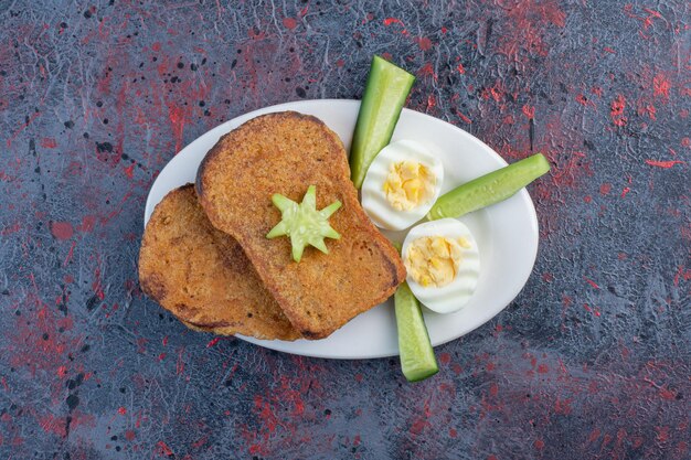 Frühstücksteller mit Eiern, Gurken und Brotscheiben.