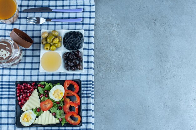Frühstückstisch aus Portionen Kaviar, Oliven, Honig, Käse, Eiern, Granatapfel, Paprika, Schokolade und Kaffee auf Marmoroberfläche