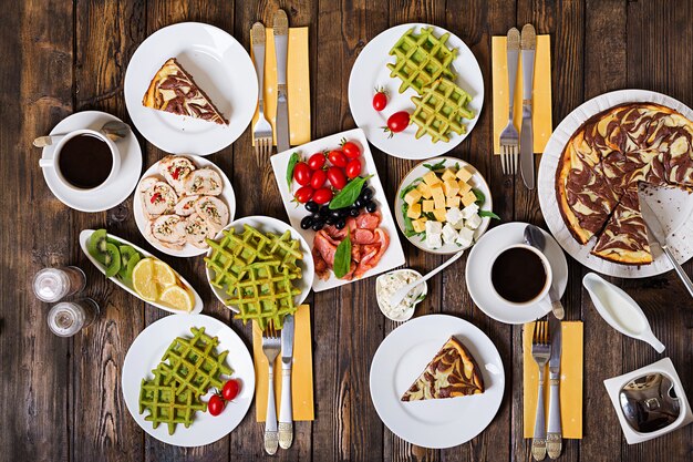 Frühstückstisch. Festliches Brunch-Set, Mahlzeit mit Spinatwaffeln, Lachs, Käse, Oliven, Hähnchenbrötchen und Käsekuchen. Draufsicht. Flach liegen