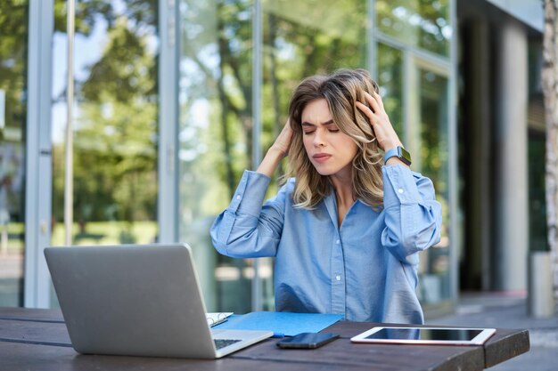 Frustrierte Geschäftsfrau, die mit Laptop auf der Straße sitzt und verärgert und enttäuscht aussieht Konzept des Versagens bei der Arbeit