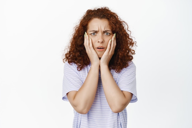 Kostenloses Foto frustrierte, schockierte frau mit lockigem haar, die die stirn runzelt und die hände im gesicht hält, zeuge eines schrecklichen unfalls, einer katastrophe, die verzweifelt vor weißem hintergrund steht