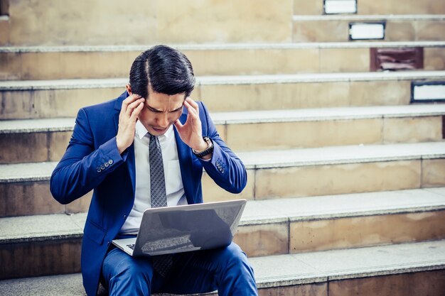 Frustrierter junger Mann, der auf dem Treppenhaus arbeitet mit Laptop sitzt. Unglückliches Problem mit der Arbeit.