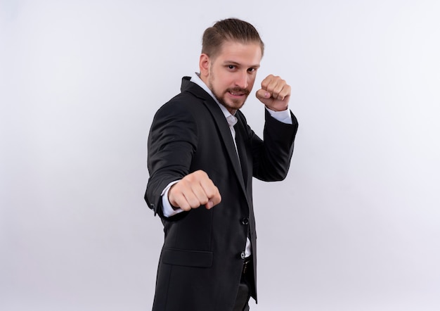 Frustrierter schöner Geschäftsmann, der Anzug geballte Fäuste trägt, die wie Boxer stehen, der über weißem Hintergrund steht