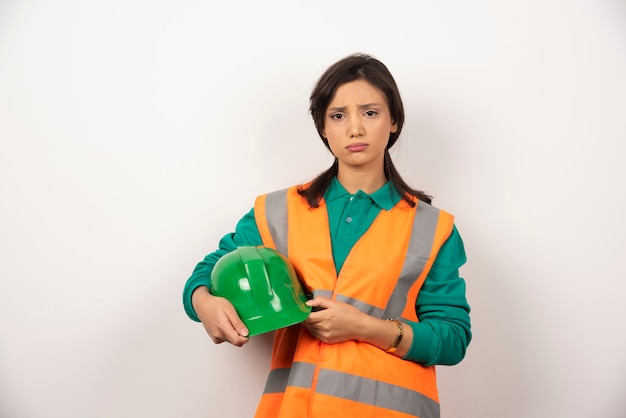 Frustrierter weiblicher Ingenieur, der einen Helm auf weißem Hintergrund hält
